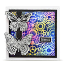 A square handmade greeting card featuring two large white laser-cut butterfly overlays on the left and a colorful patterned background with gears and circles in blue, pink, yellow, and purple. A small black label reads “DREAM BIG.