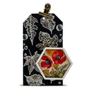 A decorative black gift tag or card insert with a gold clip at the top, featuring white leaf cutouts and a hexagonal inset showing red poppy flowers on a vintage-style background.