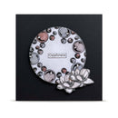 A square black card or plaque featuring a circular silver-toned design with embossed bubble patterns in metallic rose gold, silver, and black, a small central label reading 'Celebrate', and a white floral embellishment at the lower right.