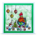 A square Christmas greeting card featuring a whimsical illustration of a rooster wearing an orange scarf, surrounded by ornaments, a decorated tree, and wrapped gifts. The card has a white border, a green inner border, and a vibrant green outer border.