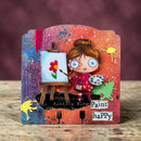 A decorative handmade art plaque featuring a cartoon girl painter holding a paintbrush and palette, with a small canvas showing a red flower. The plaque has colorful paint-splatter artwork in blue, orange, red, green, and purple, with the words 'Paint happy' on a rustic wooden surface against a dark maroon background.