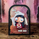 A handmade scrapbook card featuring a cute cartoon girl with dark hair, a flower in her hair, and a heart-shaped chest emblem. The card has a distressed black border, layered with pink, purple, and brown textured papers, and includes the phrases 'every stitch' and 'tells a story'.