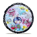 A round decorative plaque or coaster with a scalloped black edge, featuring a colorful whimsical illustration of a girl with blue hair surrounded by paint splatters, small text labels, and yarn balls on a white background.
