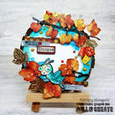 A handmade autumn-themed craft plaque displayed on a small wooden easel. The plaque features a turquoise butterfly, orange and brown leaves, metallic gold foil, and a small 'Unique' label on a white textured background.
