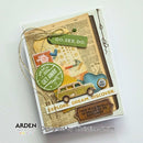 A handmade layered paper card featuring vintage travel-themed embellishments, including a green 'GO.SEE.