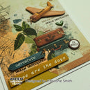A close-up of a decorative scrapbook or card design featuring vintage travel elements: a small airplane, two suitcases, leaves, a heart, and layered paper strips reading 'adventure' and 'dream destinations.' The design includes visible branding text 'ARDEN craft shows' and 'Designed by Christine Smith.