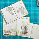 Three open handmade paper journals with mixed-media artwork and stamps, arranged on a teal cutting mat. The journals show sketches, stamps, and colorful map-like illustrations.