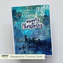 A handmade Christmas greeting card with a blue and teal abstract background, black silhouette artwork of a sleigh and deer, and the words 'Merry Christmas' in white script. The card is photographed against a light gray background with a banner at the bottom reading 'Designed by Christine Smith' and the brand 'Arden' visible in the lower-left corner.