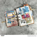 Open scrapbook with travel-themed pages on a gray surface, featuring images of a couple and a sunset.
