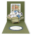 Pop-up card with a scene of two people on a couch looking out a window at deer.