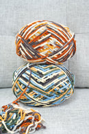 Two multicolored skeins of yarn stacked on a textured surface