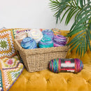 Basket of colorful yarn on a mustard yellow couch with a plant in the background