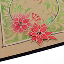 A close-up of a handmade holiday card featuring layered red poinsettia flowers with small dark blue and red rhinestone centers, set against a green and beige patterned background on a kraft cardstock.