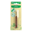 A Clover Seam Ripper tool in its original retail blister packaging. The tool features a brown handle with silver metal teeth and a clear protective cap, mounted on a light yellow backing card with green clover graphics and product details.