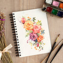 Notebook with a floral illustration, watercolor set, and brushes on a wooden surface