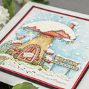 A close-up of a handmade Christmas card featuring a whimsical mushroom house in the snow, with a 'Merry Christmas' sign, textured white snow, and red and black borders.
