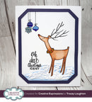 A handmade Christmas greeting card featuring a brown reindeer with antlers, blue hanging ornaments, and the text 'Oh deer Christmas already' on a white card with a navy blue border, photographed on a light wood background.