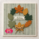An autumn-themed square card featuring layered paper leaves in orange, yellow, and green arranged in a wreath shape on a faux wood plank background. A white banner in the center reads 'Autumn,' and a pink 'Craft & You' logo appears in the lower left corner.