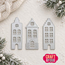 Three silver metal house-shaped die cutters arranged on a textured cream background with holiday pine branches, snowflakes, and a chunky knit scarf. A pink 'CRAFT & YOU' logo appears in the bottom right corner.