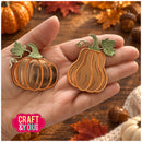 Two autumn-themed metal cutters shaped like pumpkins with green leaves and stems, held in a person's hand over a rustic fall-themed background with leaves, acorns, and small pumpkins. A pink 'CRAFT & YOU' logo is visible in the lower-left corner.