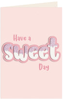 A pink greeting card with the words 'Have a Sweet Day' in stylized lettering. The word 'Sweet' is large and white with pink outlines, and the letters have a light purple glitter-like texture on top.