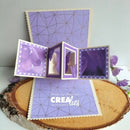 A purple and lavender 3D pop-up card set displayed on a rustic wood slice. The set includes a flat card with a geometric pattern, a folded pop-up box with butterfly details, and a larger pop-up display featuring the text 'Made by Anna for CreaLies'.