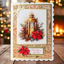 A handmade Christmas greeting card with a scalloped white border, featuring an illustration of a lantern, red poinsettias, pinecones, and vintage postage-style stamps. The card is displayed on a wooden surface with a warm, blurred holiday background.