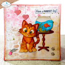 A handmade greeting card featuring a cute orange tabby kitten sitting next to a fishbowl with a goldfish, with pink hearts hanging in the background and the text 'Have a PURRFT day!' at the top. The card is shown standing upright on a speckled countertop.