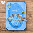 A handmade layered card featuring two 3D bird cutouts on a blue oval background with butterflies and the phrase 'in the garden of time bloom at your own pace.' The card is photographed flat on a wooden surface, with a 'Elizabeth craft designs' logo in the top-left corner.