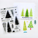 A set of Christmas tree-themed craft supplies on a white background, including a clear stamp sheet with black tree and holiday motifs, a white card stamped with green trees, and several small tree stickers in different green shades.