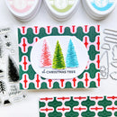 A handmade Christmas card featuring three textured Christmas trees in red, green, and blue on a white oval, set against a green and red patterned card. The card is displayed on a white background with crafting supplies, including stamping tools and ink pads.