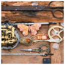 Steampunk-style decorative objects arranged on a rustic wooden surface, including a butterfly-shaped piece, a beetle-shaped piece, a spoon with a coiled object, gears, scissors, and clockwork parts.