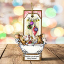 A handmade Christmas ornament featuring two cartoon mice in a bathtub with ornaments hanging above them, displayed on a wooden surface with a colorful blurred holiday bokeh background.
