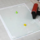 Small green and yellow objects on a clear acrylic sheet with a red and black tool.