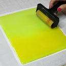 Person using a roller to smooth out a sheet of yellow material on a white surface.
