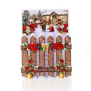 A Christmas-themed greeting card or decorative sign featuring a snowy wooden fence with red poinsettias, a gold bow, small decorated trees, and a winter village scene printed at the top. The front reads 'Snowy Days Christmas Wishes'.