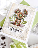 A handmade greeting card featuring a stamped sunflower arrangement in a pot with the words 'GRATEFUL for you' on an embossed cream background, styled with green and white cardstock and craft tools.