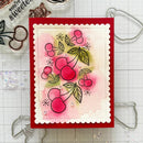 A handmade greeting card featuring a cherry illustration, displayed on a gridded craft mat with metal cutters and clear stamps around it.
