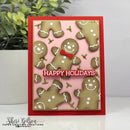 A handmade Christmas greeting card featuring gingerbread men on a pink background with a red border and the text 'HAPPY HOLIDAYS' in white. The card is displayed on a white surface with a potted plant in the background.