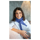 A smiling woman with curly brown hair wearing a textured blue knit scarf and a white top, seated indoors with a neutral gray and beige background.