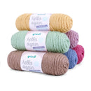Three skeins of Grundl Hello Again yarn stacked on a white background, showing the mustard yellow, mint green, and taupe colors, with additional purple, blue, and pink skeins partially visible behind them.