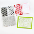 A flat lay of crafting supplies on a white background, including a clear stamp set with black and white patterns and text, a red and white striped card, a pale pink card with heart shapes, and a green card with printed text.