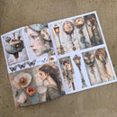An open art print or sticker album spread on a textured beige surface, featuring vintage-style illustrations including a woman's profile, flowers, butterflies, street lamps, and birds in muted pastel tones.