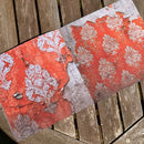 A rectangular decorative board or tray featuring a distressed red and white damask pattern, photographed diagonally on weathered wooden slats.