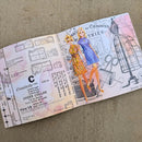 A vintage-style fashion booklet or pattern booklet spread open on a beige fabric surface. The pages feature illustrated fashion dolls in dresses, sewing machine drawings, sizing diagrams, and printed text including 'Craavates' and 'Under Collar'.