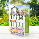 Greeting card with garden scene, flowers, and a bird on a white picket fence.