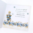 An open white greeting card featuring a decorative nutcracker illustration in blue and gold, blue poinsettia flowers along the bottom, and printed holiday text on the front.