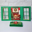 A green Christmas-themed card game set displayed on a white surface against a white brick wall. The set includes an open triptych-style card frame with gold-trimmed window cutouts and a central holiday scene, plus a matching green box with a red poinsettia and green leaf embellishment.