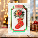 A festive Christmas greeting card displayed on a wooden surface, featuring a red patterned stocking filled with green pine branches, red poinsettias, and wrapped gifts, set against a sheet music background with warm bokeh lights.