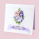 A handmade greeting card featuring a 3D floral bouquet of pink and purple bell flowers with green leaves, accented by a purple ribbon bow and a small label reading 'Bell Flower', set against a solid pink background.